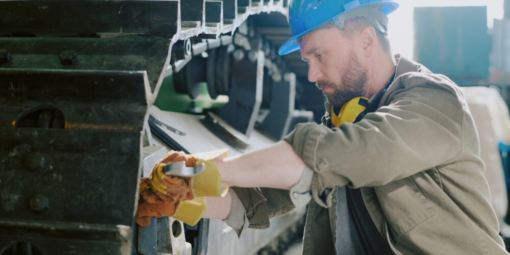 Medium shot of Caucasian male mechanic using wrench while repairing bulldozer undercarriage, copy space