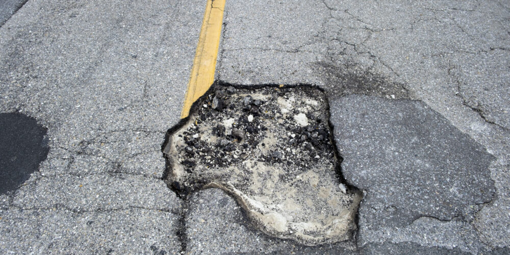 Damaged asphalt road with deep pothole on american highway surface. Ruined roadway in urgent need of repair.