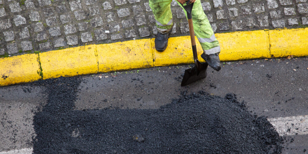 Worker with a shovel taking a break during the repair of a road with asphalt on city street. High angle view